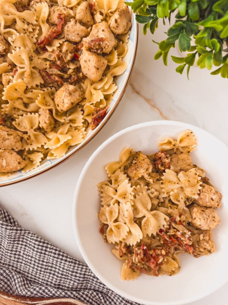 A white bowl with chicken pesto pasta and a skillet with more of the pasta.