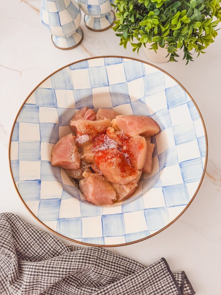 Chicken cubes being tossed in spices in a blue checkered bowl.