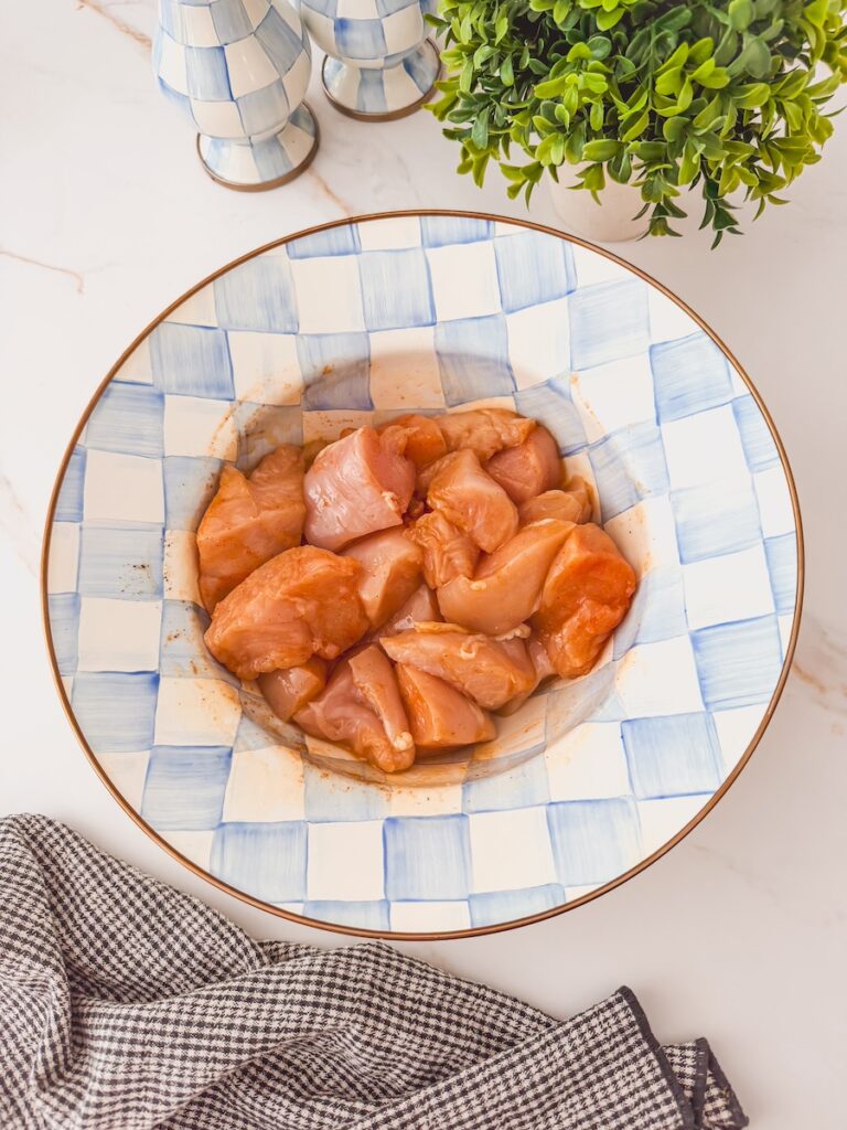 A blue checkered bowl with chicken breast cubes tossed in spices.