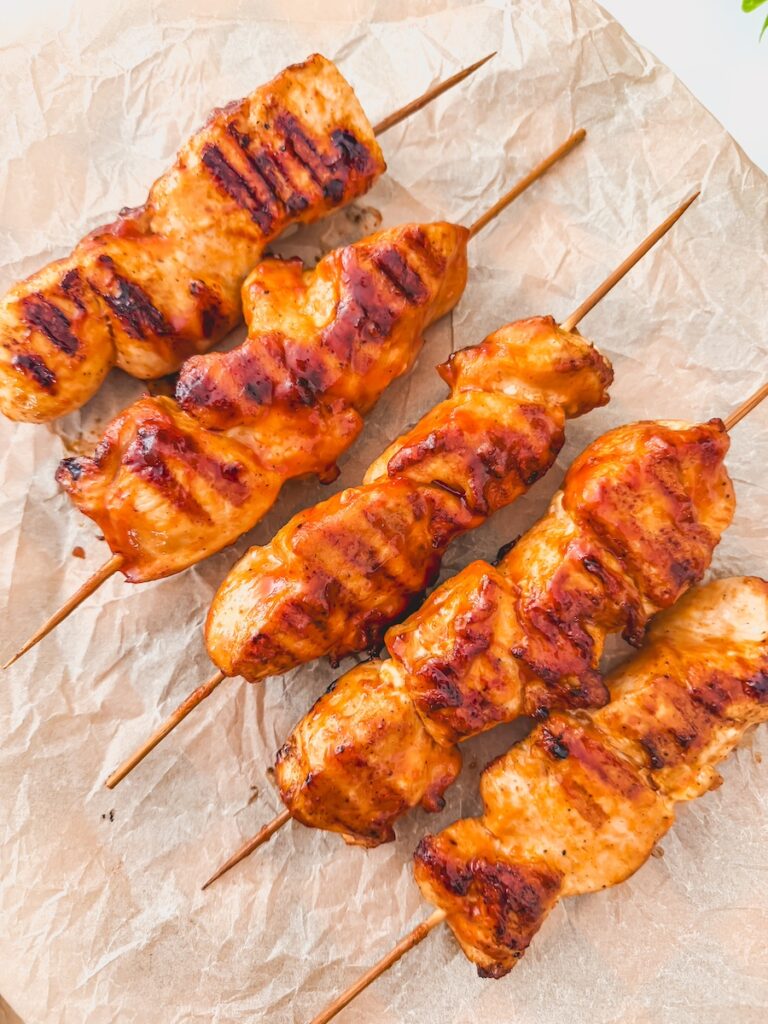 Chicken skewers on a stick grilled with barbecue sauce. The skewers are on a crumbled piece of parchment.