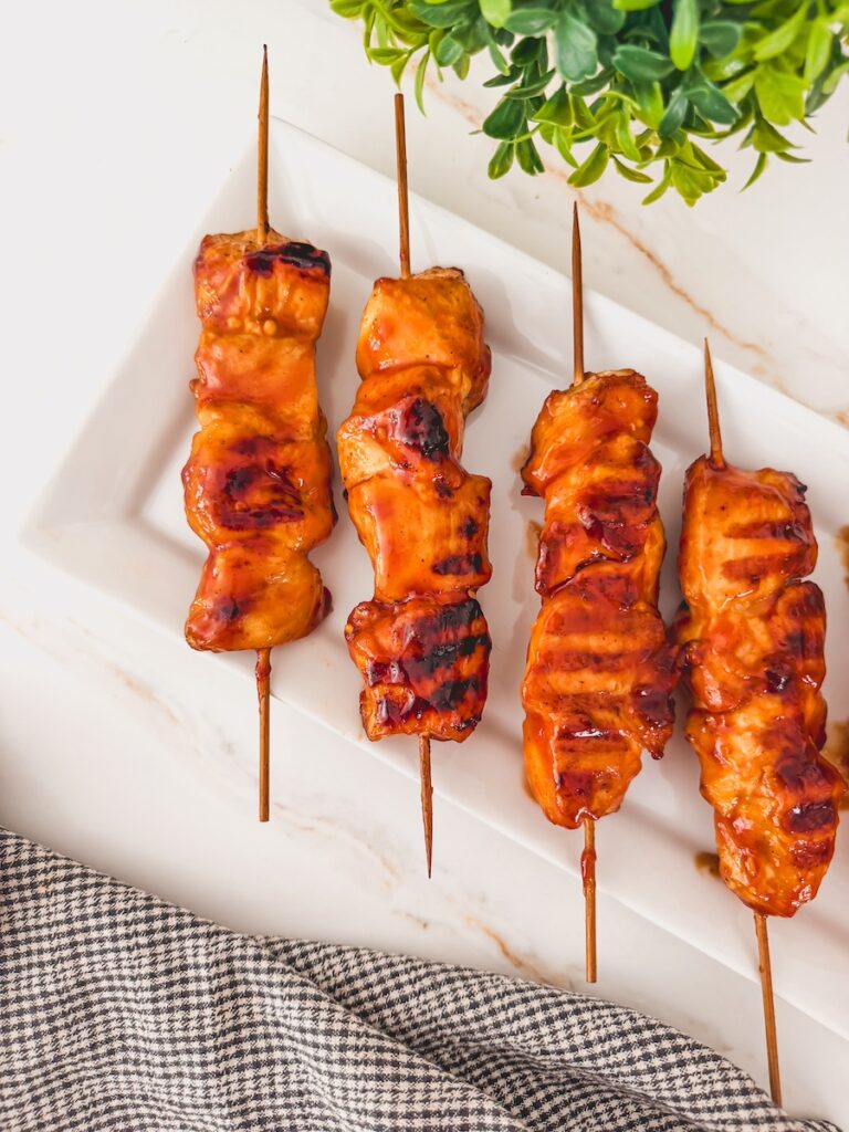 Grilled barbecue chicken skewers on a white plate.