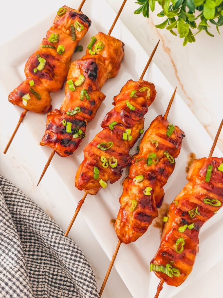 Grilled barbecue chicken skewers on a white plate.