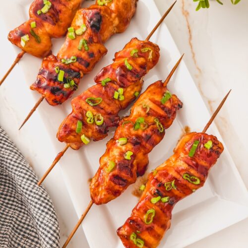 Overhead image of bbq chicken kebabs on a white plate.