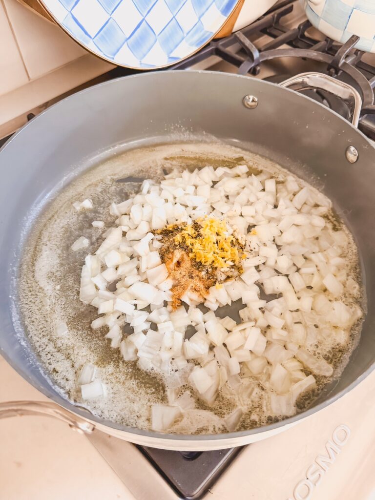 A skillet with onion, garlic, and spices cooking in butter.