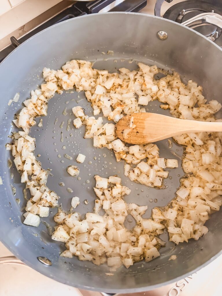 A skillet with onion, garlic, and spices cooking.