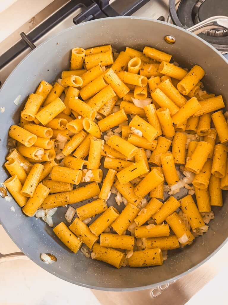 A pan with pasta noodles, onion, garlic, and spices.