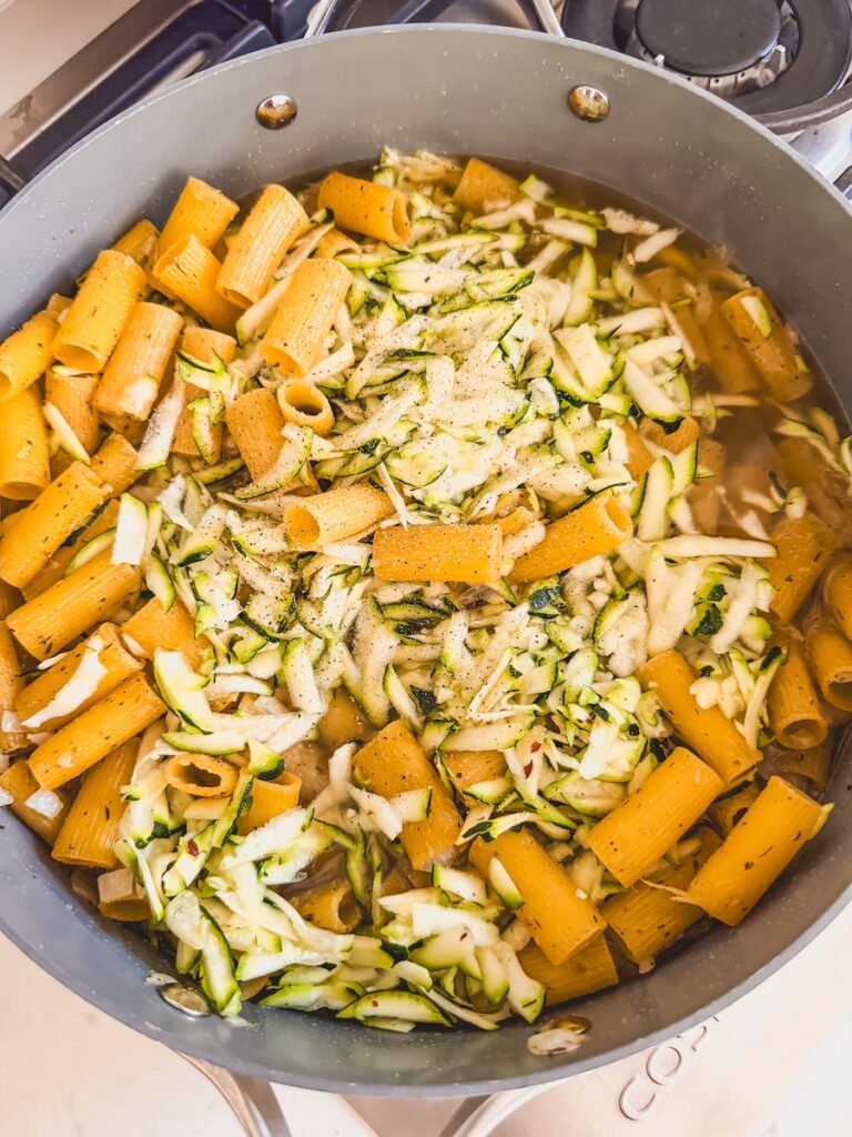 A pan with grated zucchini, pasta, and stock.