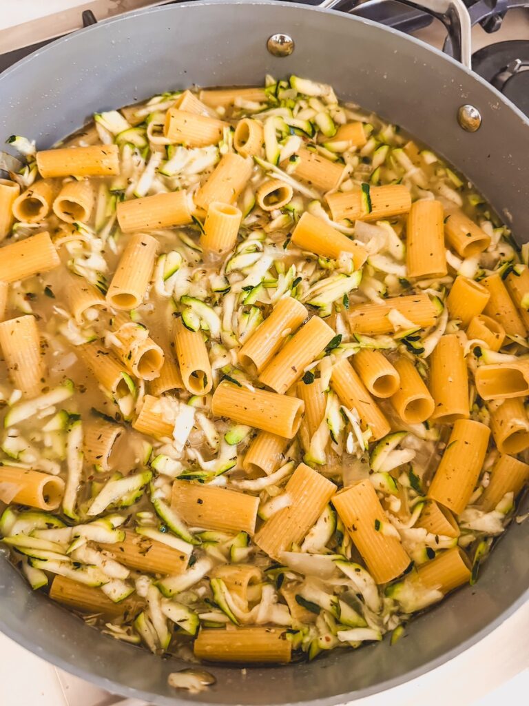 A pan with zucchini, pasta, and stock.