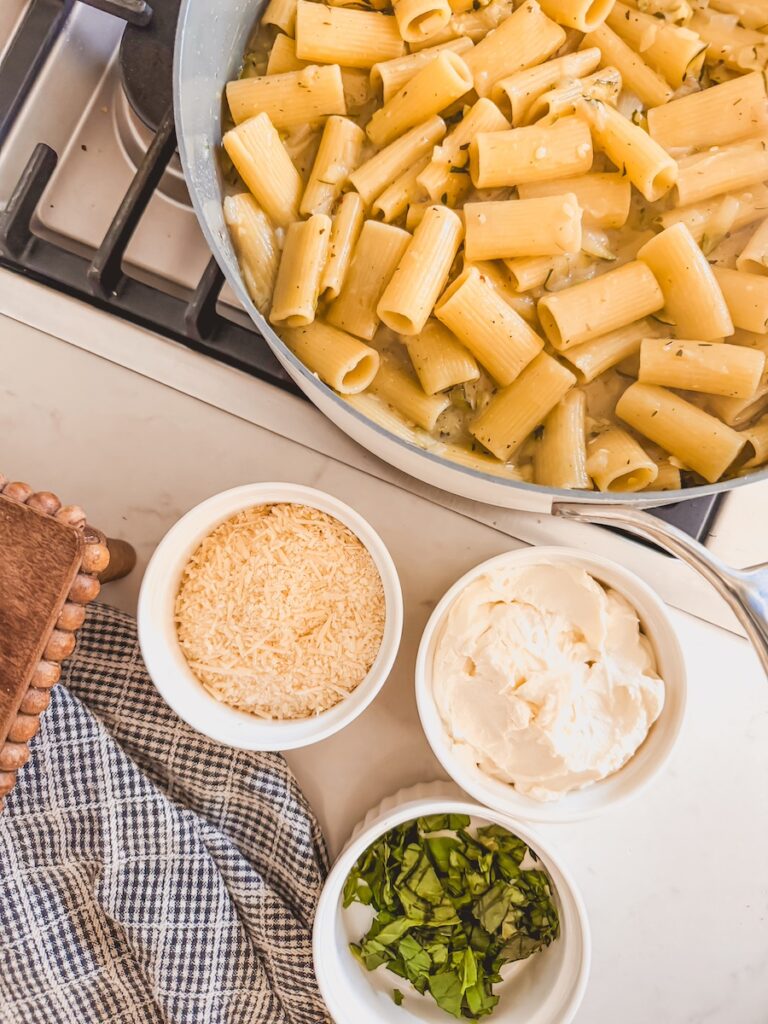 Overhead image of a pan with noodles and zucchini, cheese, ricotta, and basil.