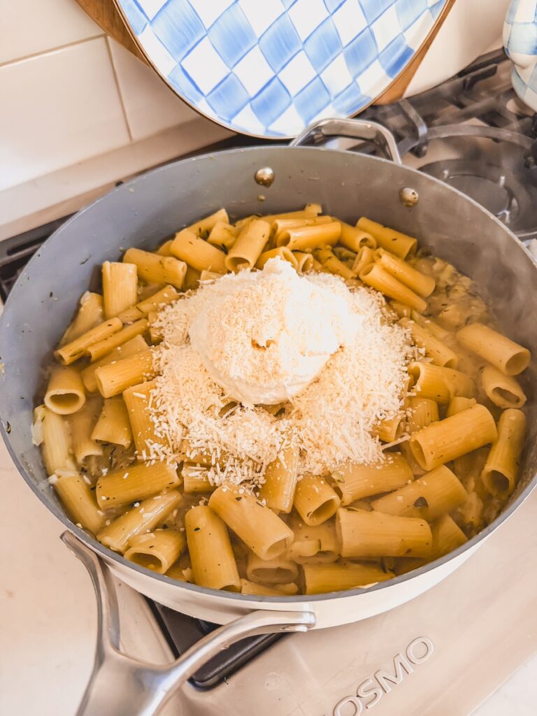 A skillet with lemon zucchini pasta with ricotta and cheese on top.