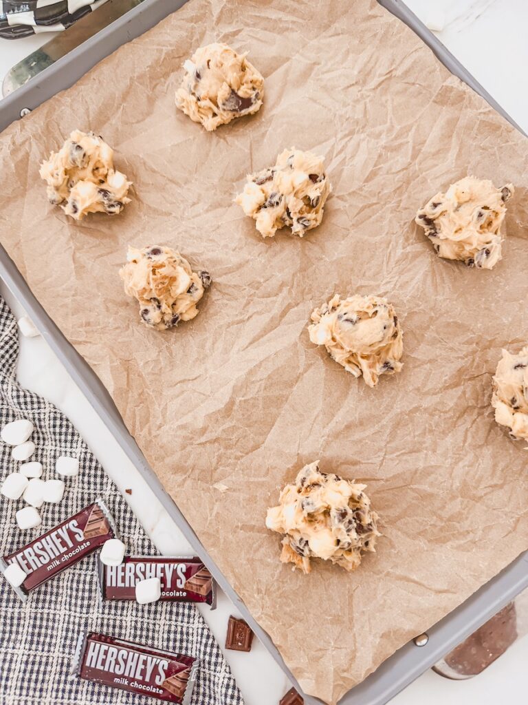A baking sheet with parchment paper and scoops of smores cookie dough.