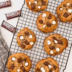 Smores cookies on a black wire cooling rack with hersheys chocolate bars to the left side.