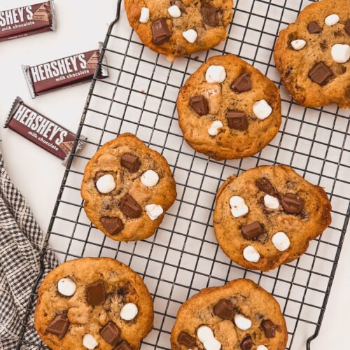 Smores cookies on a black wire cooling rack with hersheys chocolate bars to the left side.