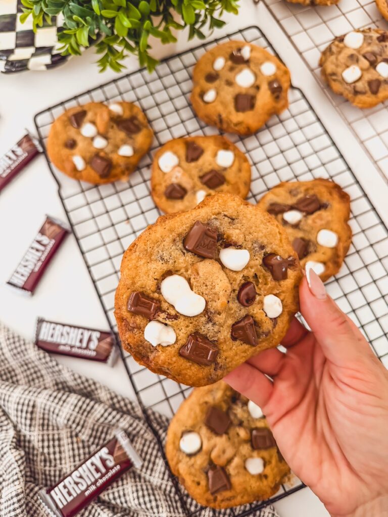 A hand holding a smores cookie above others on a black cooling rack.