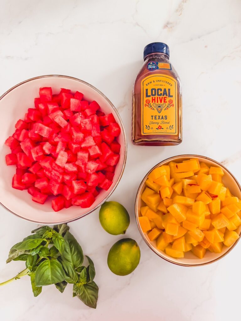 flatlay of ingredients for watermelon peach feta salad; watermelon, peaches, feta, honey, lime juice, and basil