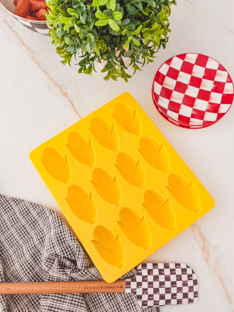 empty corn dog mold on counter next to checked side plate and dish towel