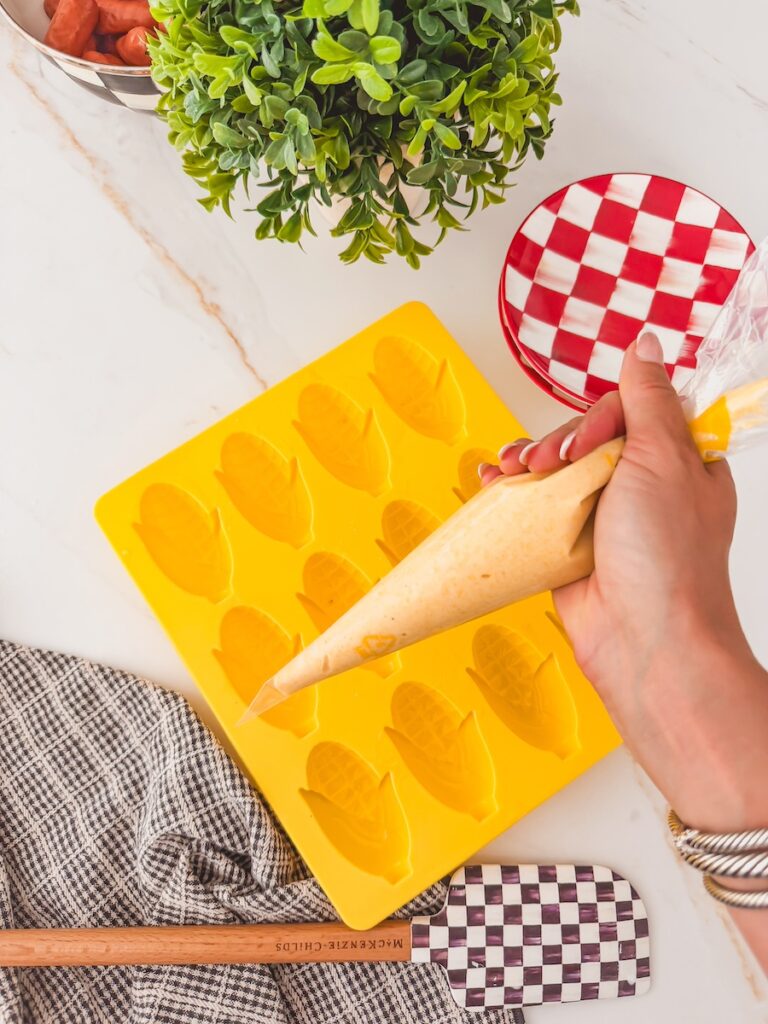 hand holding piping bag of batter ready to fill mold in the background