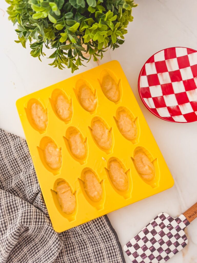 yellow corn dog mold filled with batter on counter with red and white checked plate and dish towel next to it.