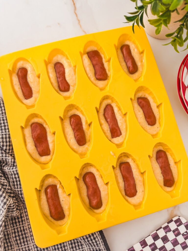 filled mold of corndogs with hot dogs placed into batter