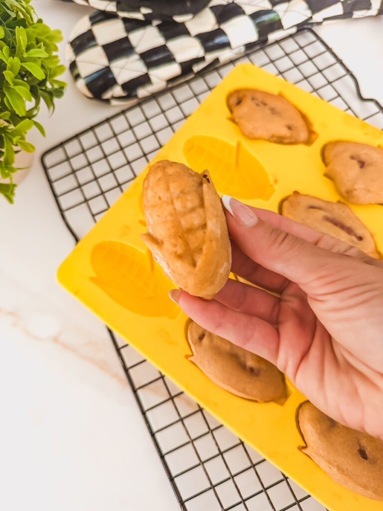 hand holding corndog out of mold. mold of baked corndogs in background on rack.
