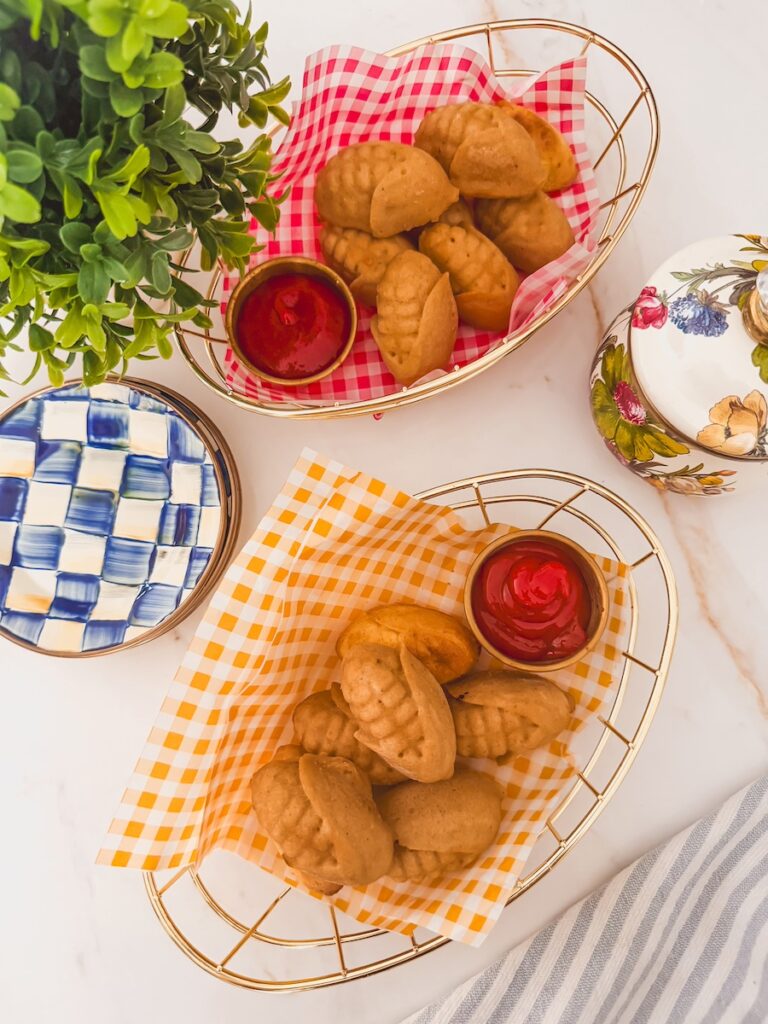 wider shot of overhead shot of finished corn dogs in baskets with checked paper and ramekins of ketchup. side plates to the side.