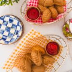 overhead shot of finished corn dogs in baskets with checked paper and ramekins of ketchup. side plates to the side.