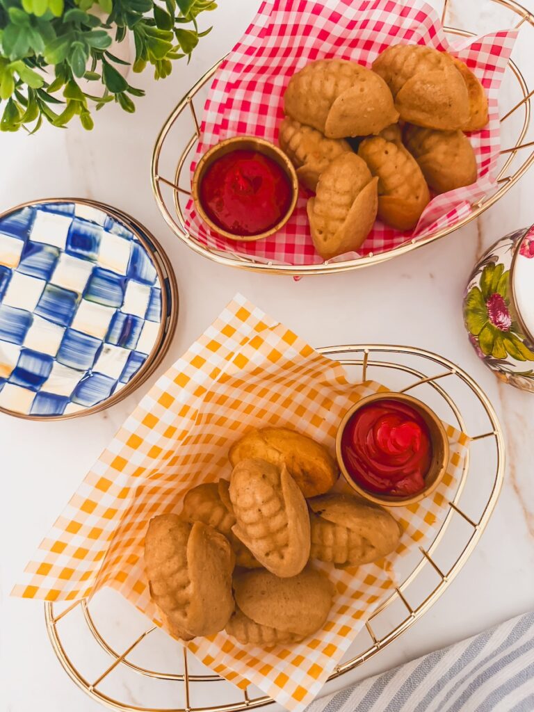 overhead shot of finished corn dogs in baskets with checked paper and ramekins of ketchup. side plates to the side.