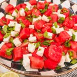 Finished and plated watermelon feta mint salad in black and white checked serving bowl with lime halve on side of bowl.