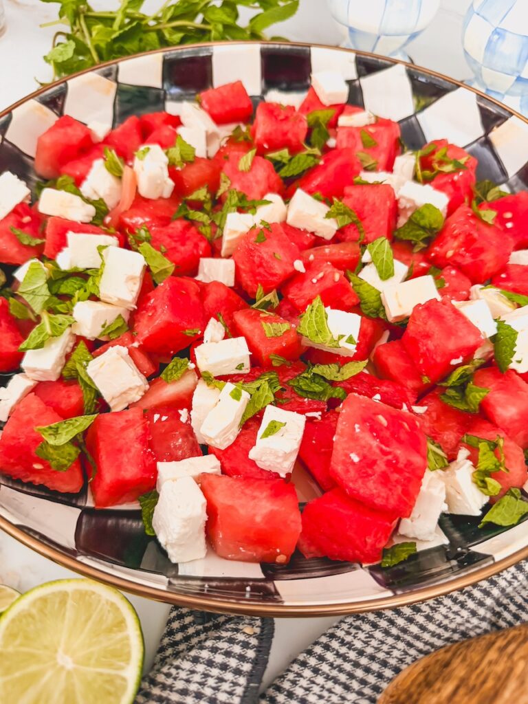 Finished and plated watermelon feta mint salad in black and white checked serving bowl with lime halve on side of bowl.