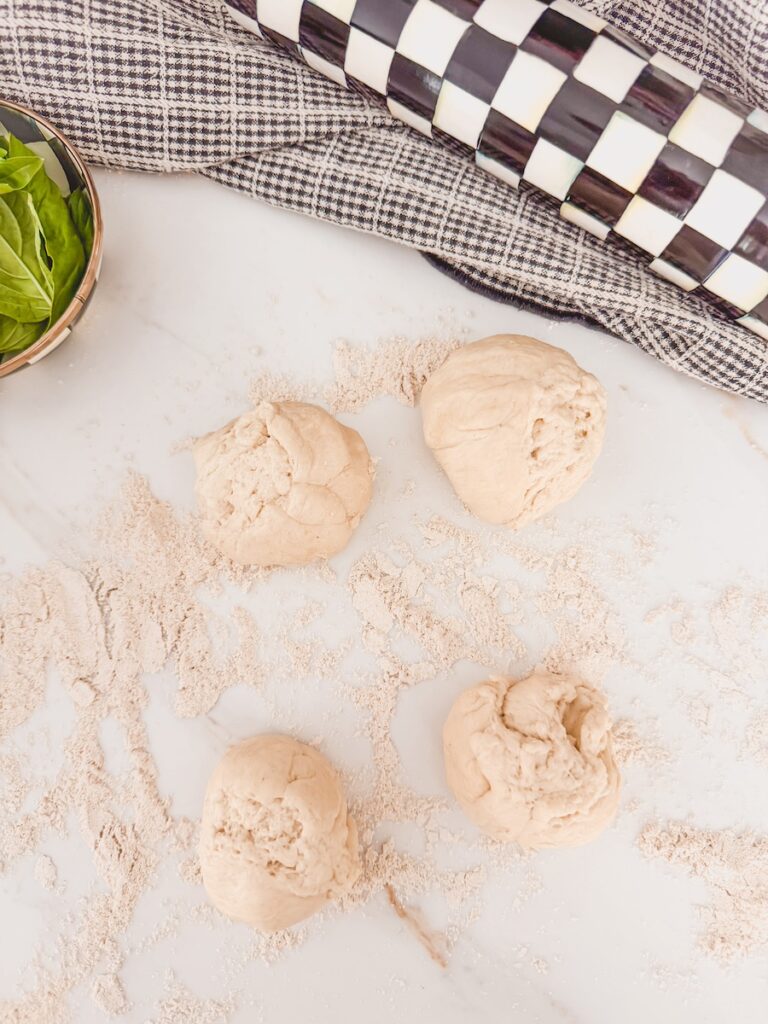 Pizza dough shaped into 4 balls with a checkered rolling pin to the side nad a checkered linen.