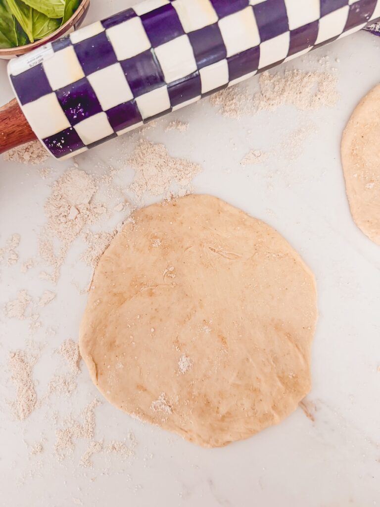 Individual pizzas are rolled out on a floured surface with a checkered rolling pin.