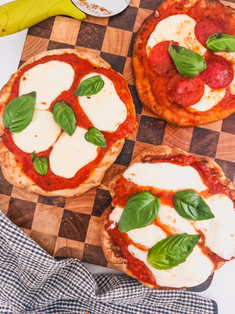 Overhead image of three grilled pizzas on a checkered cutting board.
