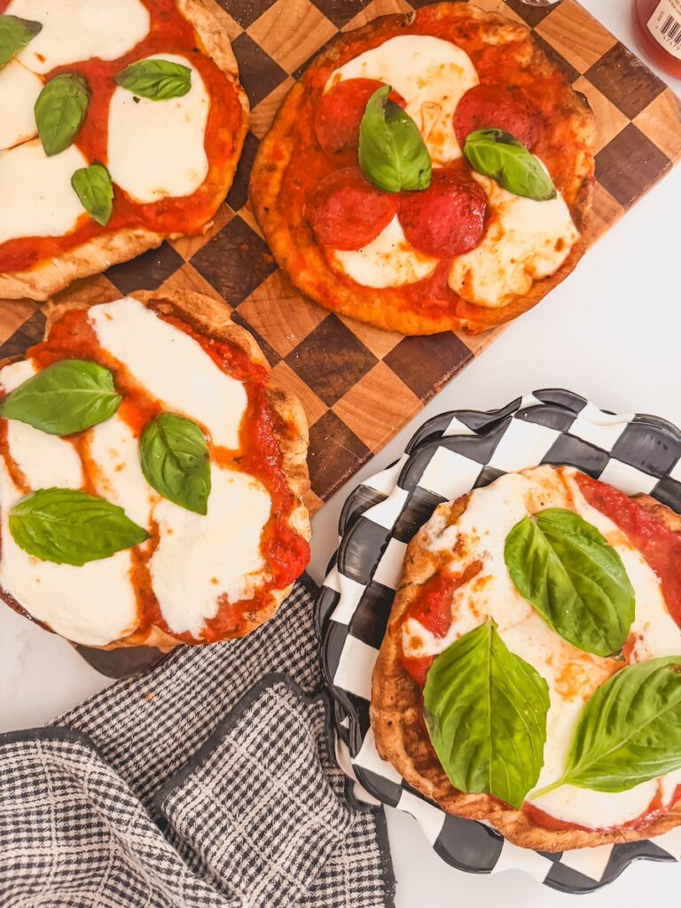 Overhead image of grilled pizzas on a checkered cutting board. One of the pizzas is on a checkered black and white plate.