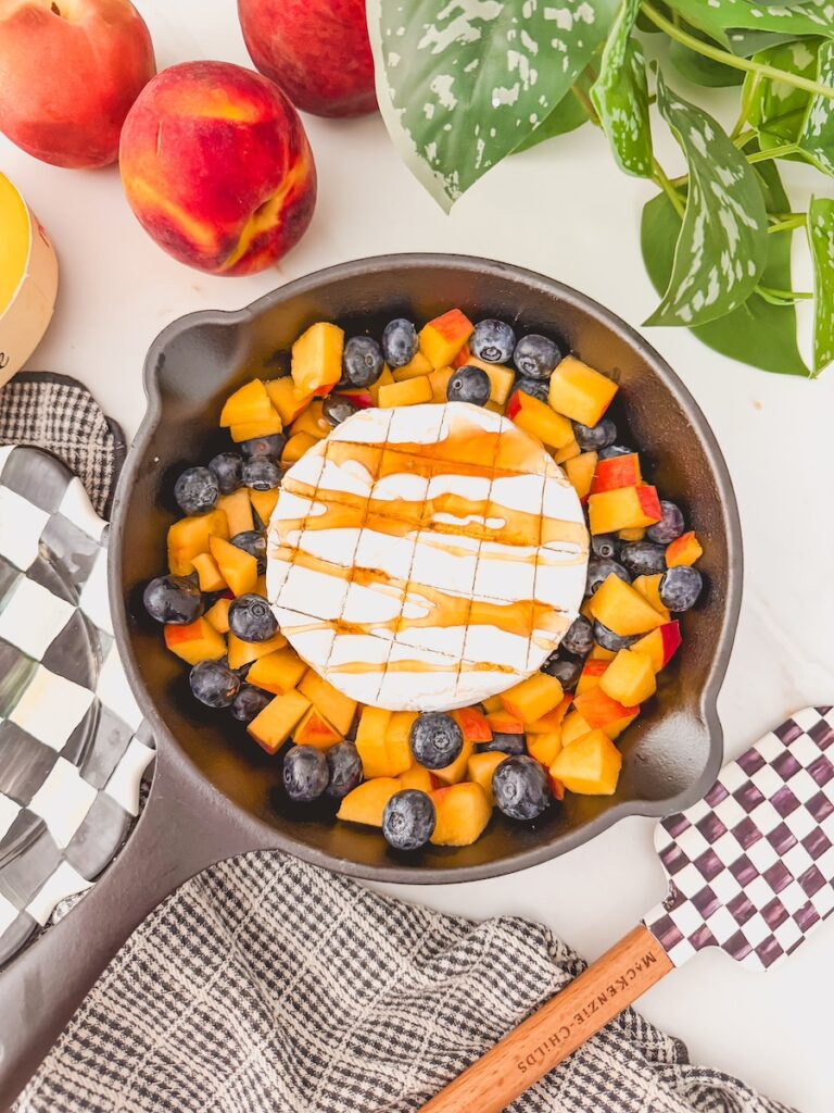 drizzle of honey on brie in skillet with blueberries and peaches