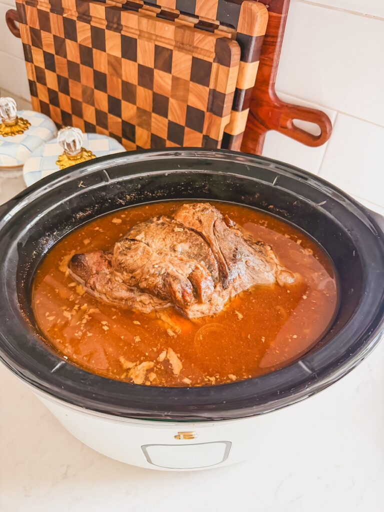 cooked pork butt in slow cooker with juices and sauce