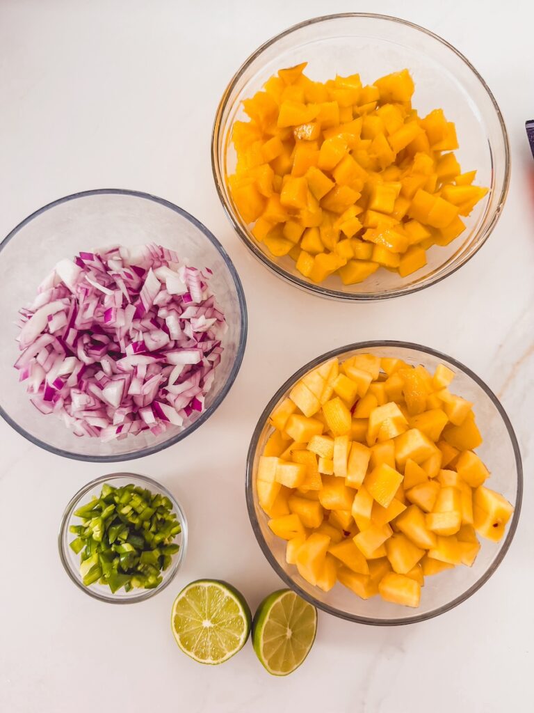 mango peach salsa ingredients in glass bowls; mango , peach, red onion, jalapeno, lime