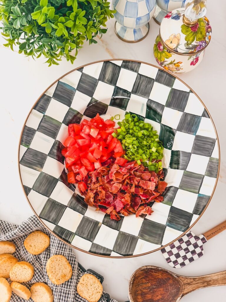 chopped bacon, tomatoes and lettuce in black and white serving bowl. crostini and serving utensils on the side.