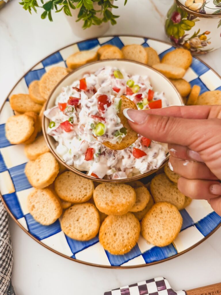 hand holding crostini that's been dipped into blt dip. blt dip platter in background.