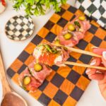 a piece of charcuterie sushi with prosciutto, salami, burrata, arugula, roasted red pepper