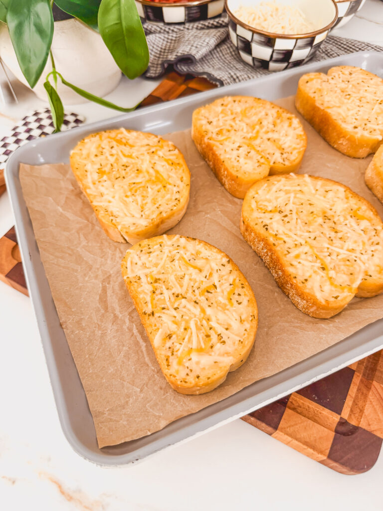 toasts on sheet tray topped with cheese, on top of cutting board