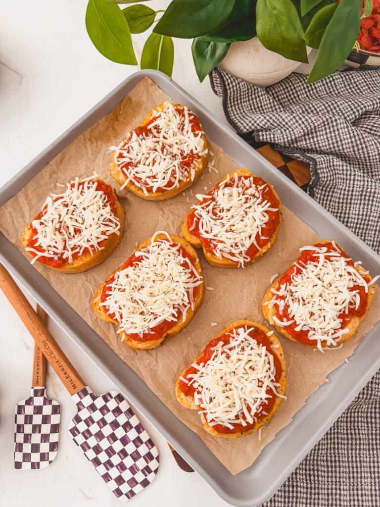toasts on sheet tray topped with sauce and mozzarella