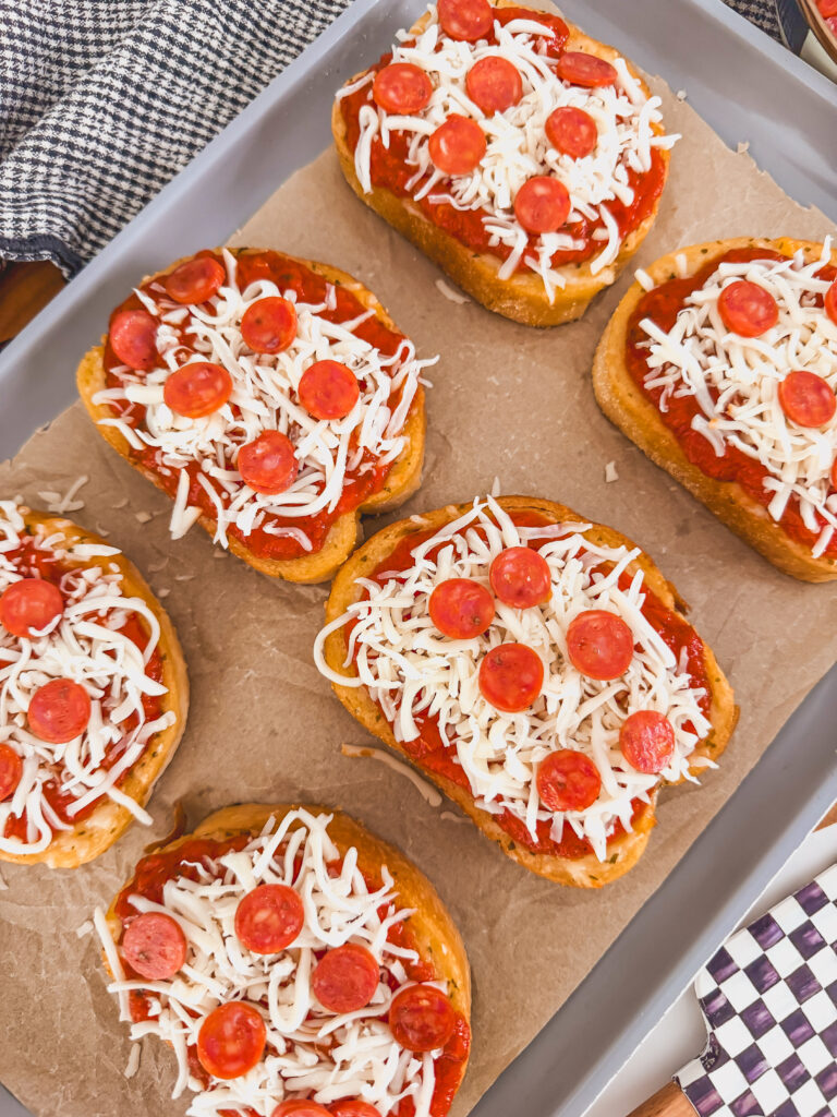toasts on sheet tray topped with sauce, mozzarella and mini pepperonis