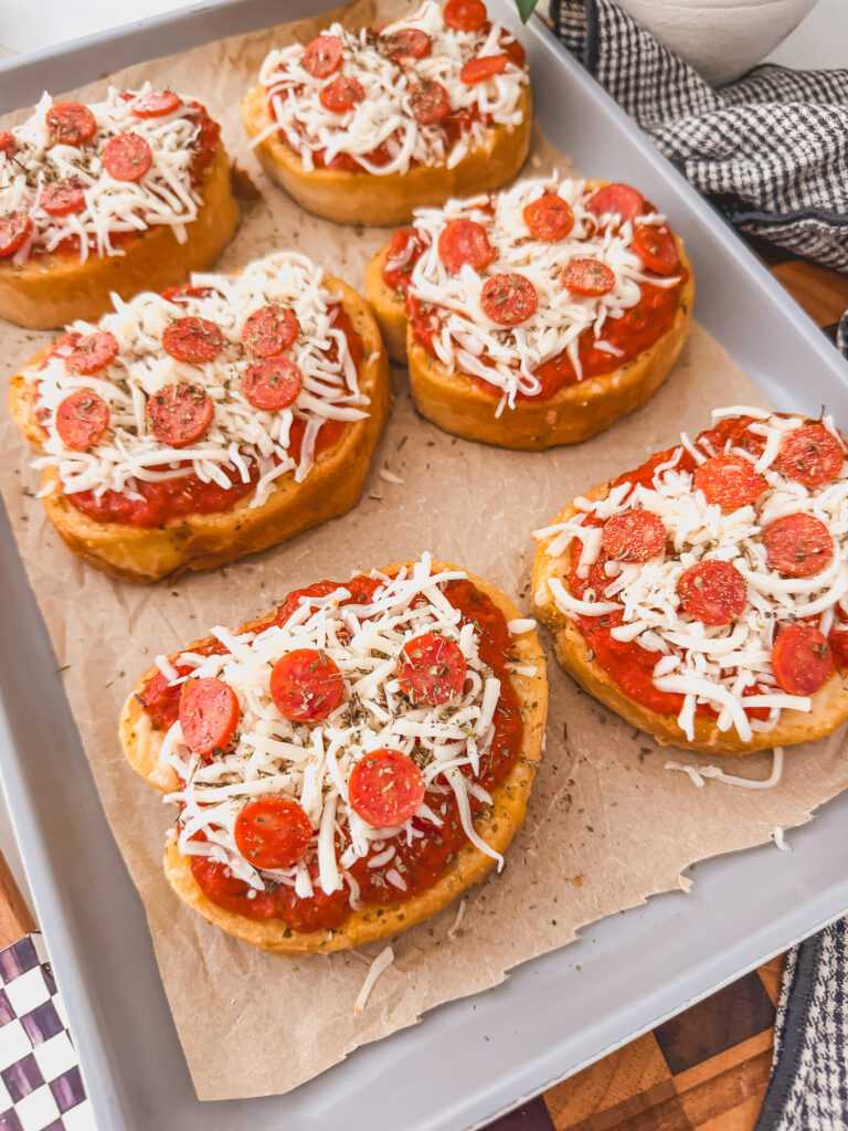 toasts on sheet tray topped with sauce, mozzarella and mini pepperonis, and italian seasoning