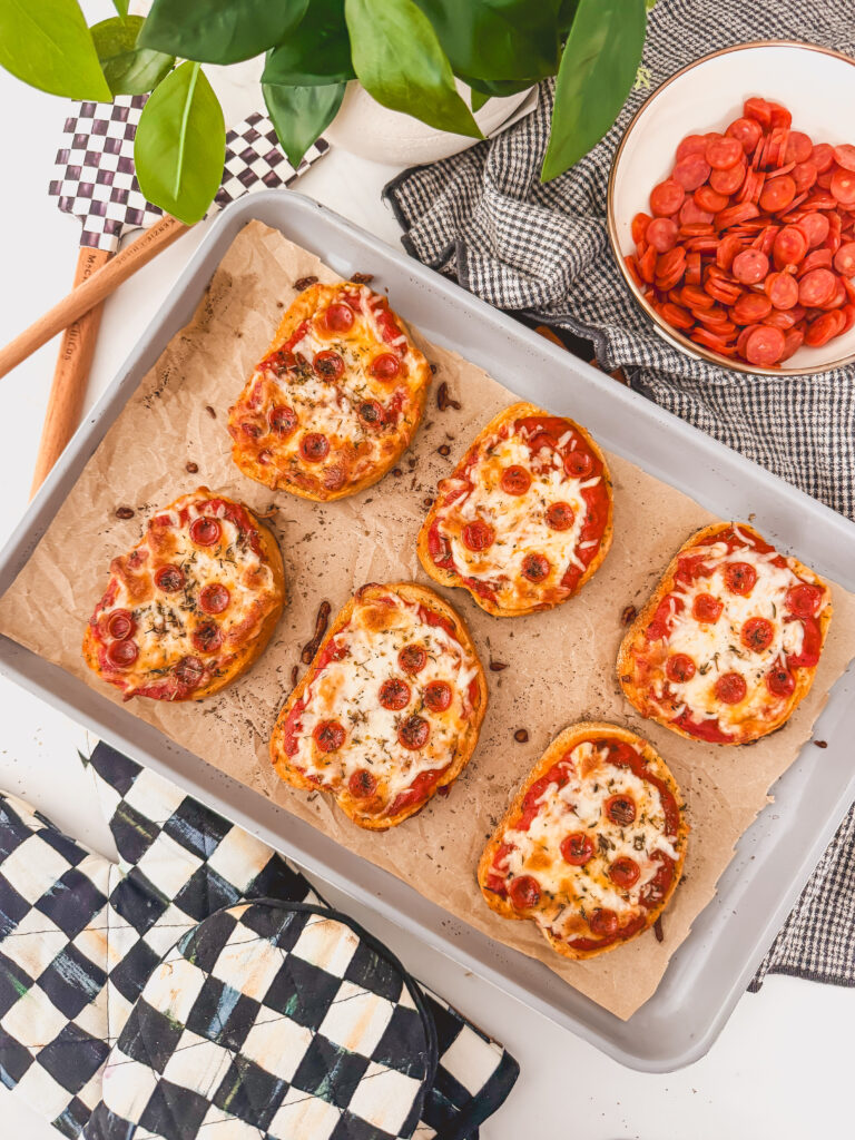 birds eye view of baked pizza toasts on sheet tray next to bowl of pepperoni