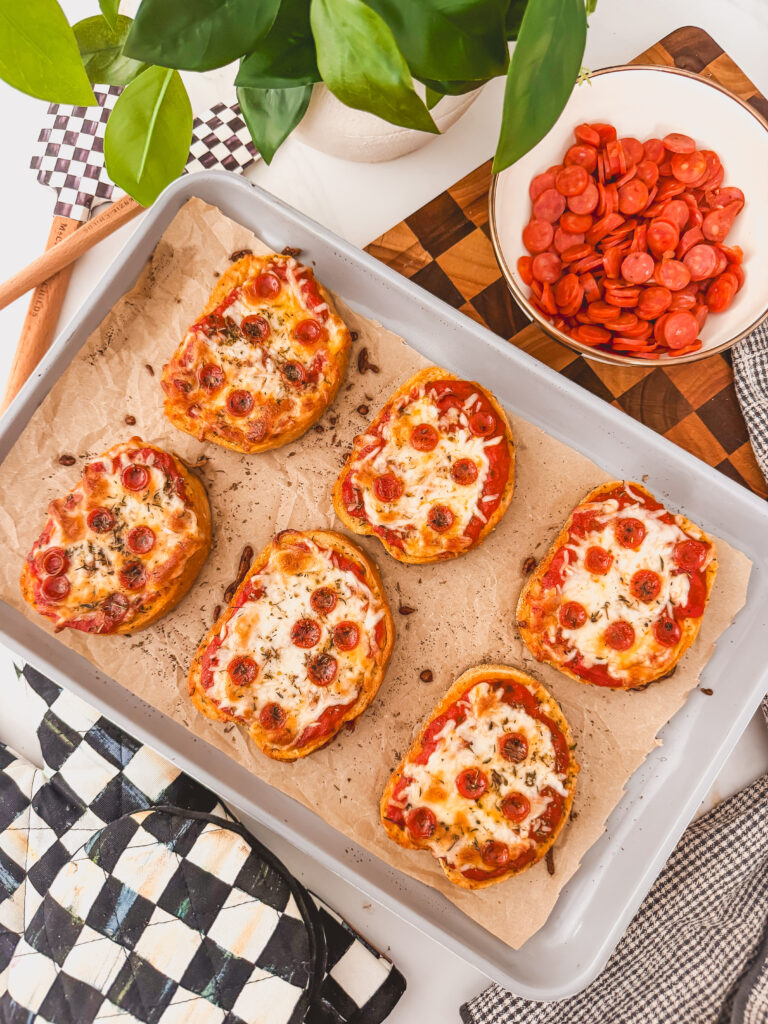 a slightly different view of birds eye view of baked pizza toasts on sheet tray next to bowl of pepperoni
