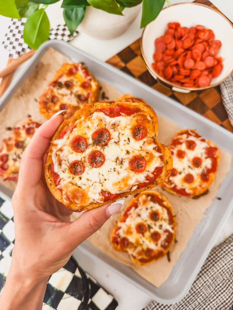 left hand holding baked pizza toast with pizza toasts on sheet tray in background