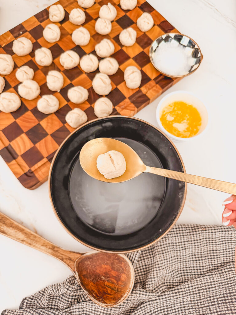 biscuit dough balls on cutting board in background with bowl of baking soda mixture and spoon holding biscuit dough ball