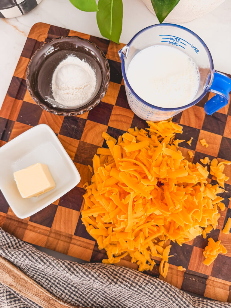 shredded cheddar cheese, pat of butter, flour and milk on cutting board