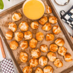 overhead view of baked biscuit pretzel bites on sheet tray with cheese sauce, with checkered spoon on the side