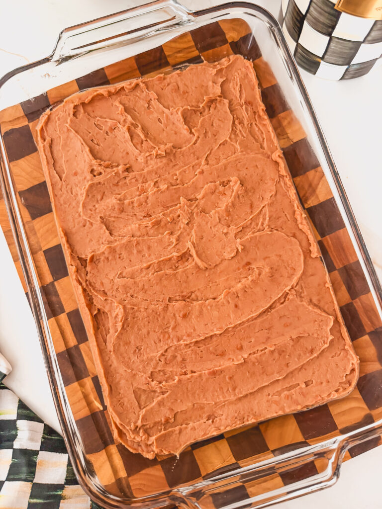 Overhead image with refried beans in the bottom of a glass baking dish.